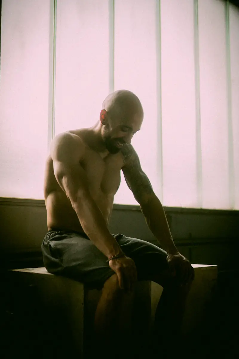 topless man in black denim jeans sitting on black wooden table