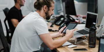 man holding turned-on iPad in front of turned-off MacBook Air